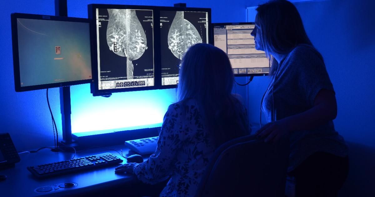 two women in dark office with blue light viewing scans on screens