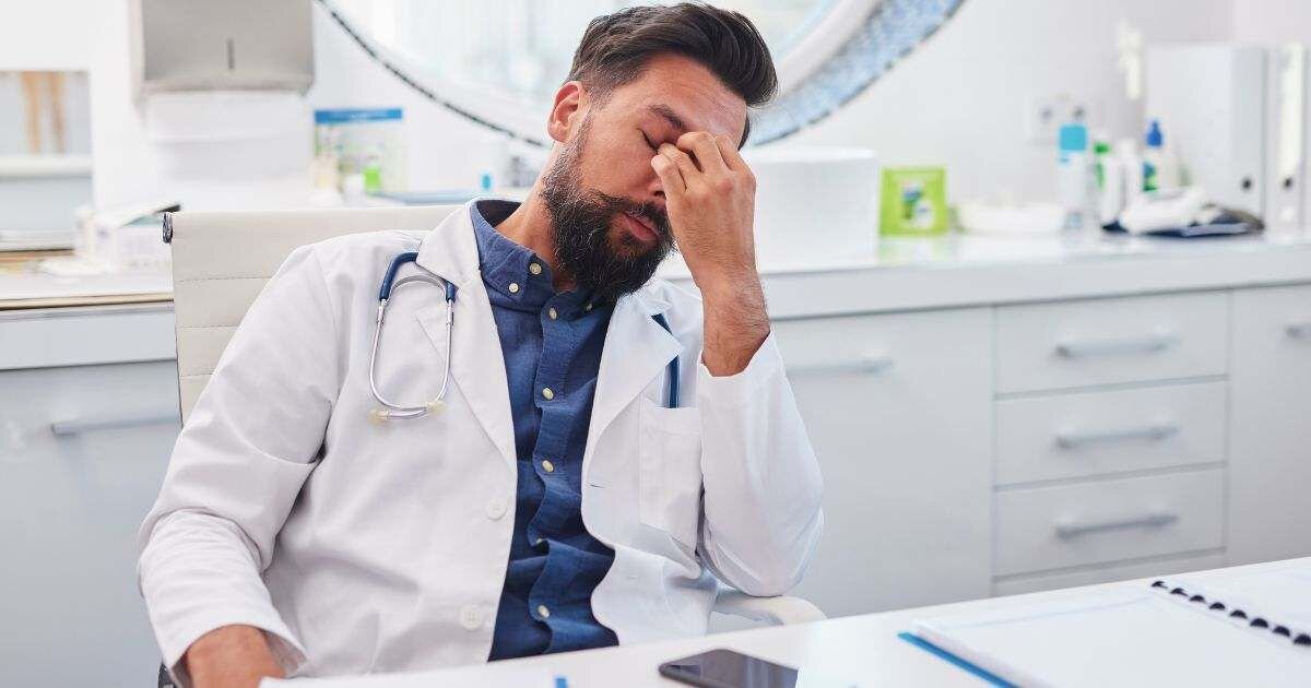 doctor sitting at desk seeming stressed holding his eyes 