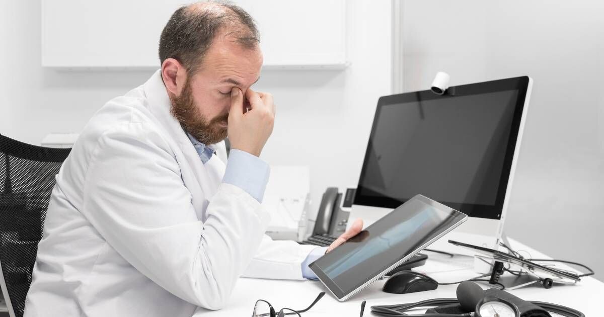 doctor sitting at desk seeming stressed holding eyes