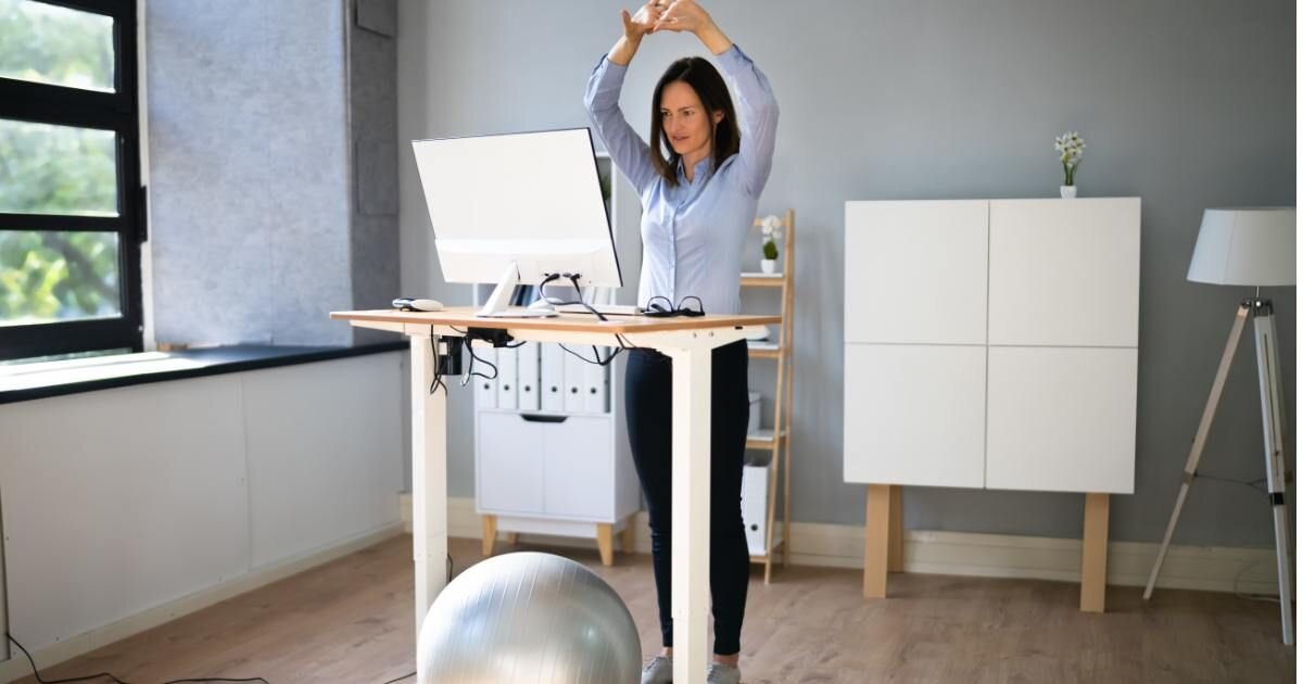 women standing while stretching her arms in front of sit to stand desk